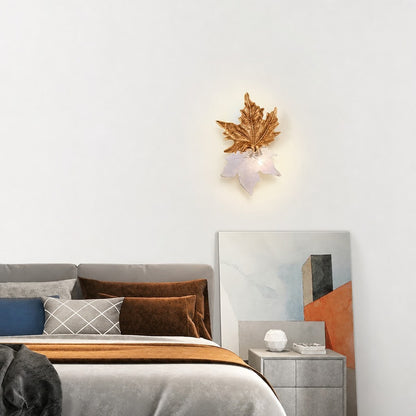 Lit maple leaf sconce in gold and pale glass above a bed with rust and grey pillows