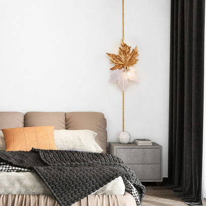 Maple leaf sconce on slim brass rod against white bedroom wall near dark curtains
