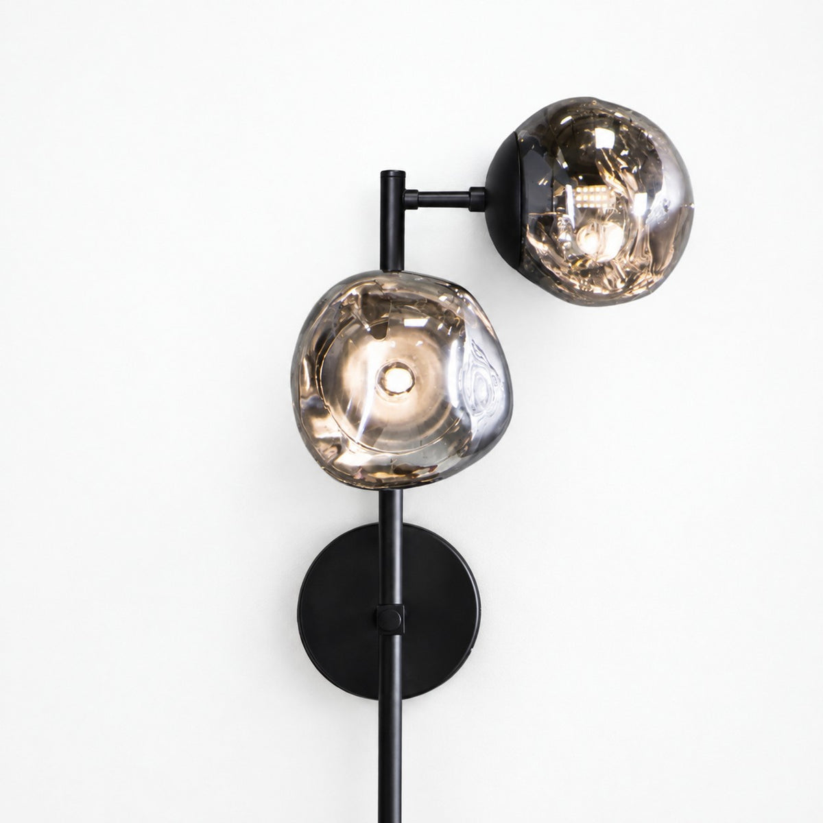 Lit twin smoked glass globes on matte black stem and disc backplate against pale wall