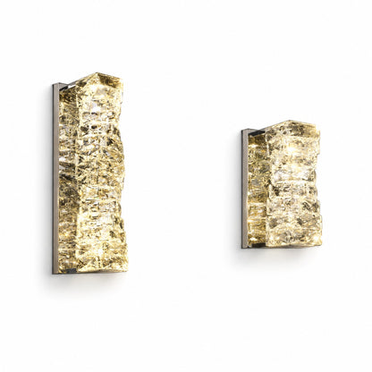 Two lit crystal sconces side by side on white wall, tall and compact sizes