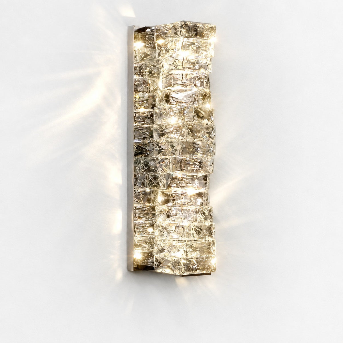 Frontal view of lit tall sconce, chrome backplate and stacked crystals casting soft shadows