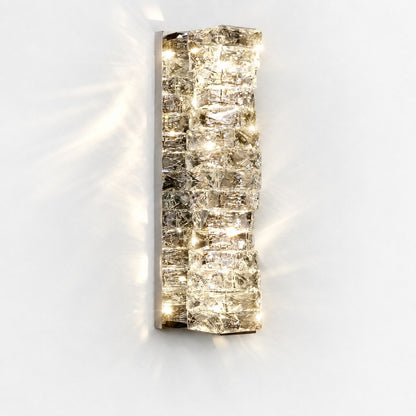 Frontal view of lit tall sconce, chrome backplate and stacked crystals casting soft shadows