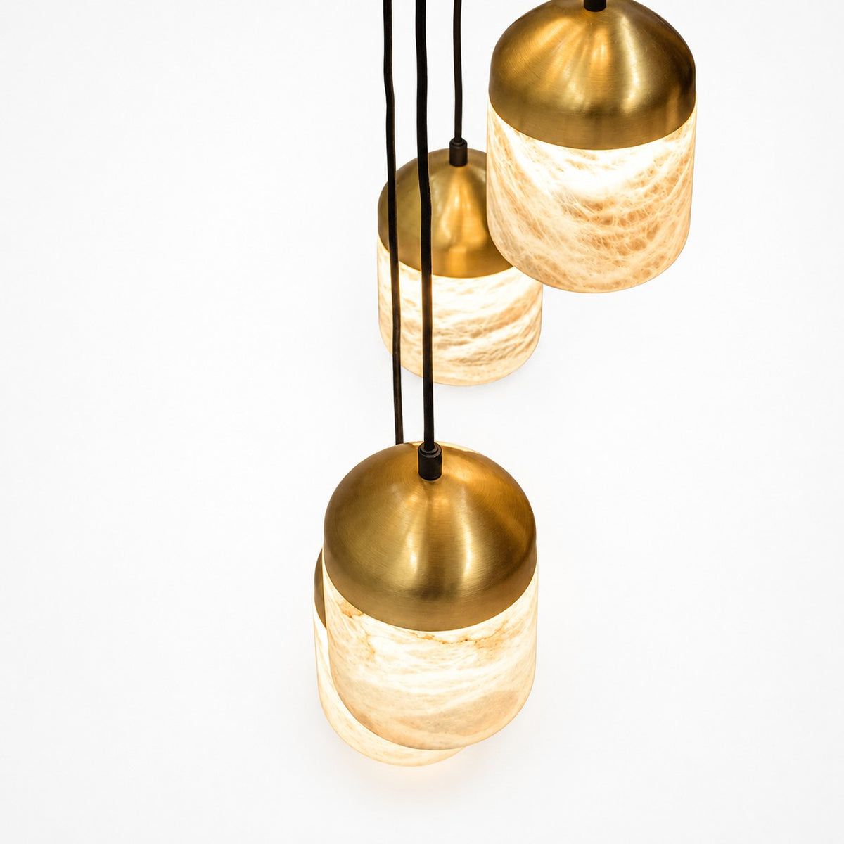 Close-up of three lit pendants, domed brass caps glowing over veined alabaster shades
