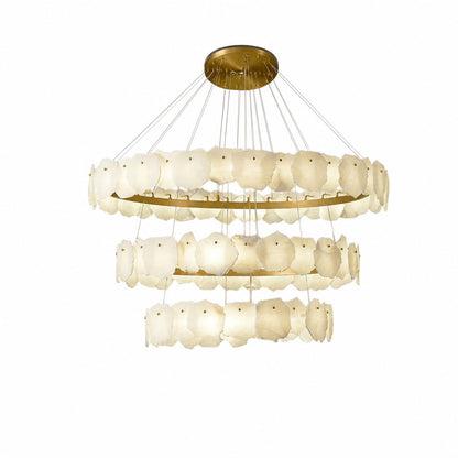 Angled view of three-tier chandelier, warm cream stone tiles glowing against brushed brass frames