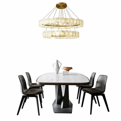 Two-tier chandelier hanging above marble dining table with dark leather chairs and ceramic vase