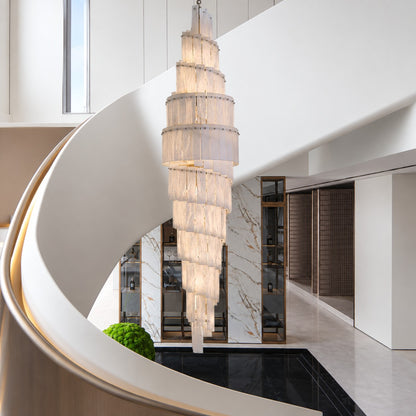 Spiral alabaster chandelier cascading beside a curved white staircase in a bright marble entry hall